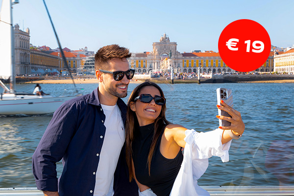 A joyful selfie of a young couple on a Tejo River cruise in Lisbon with the Praça do Comércio in the background